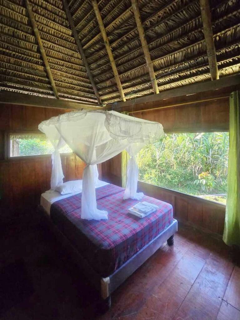 A view of a large bed with mosquito netting and views outdoors at Cuyabeno Kichwa Lodge.